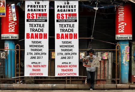 A man reads a newspaper next to banners in front of a closed garments market, during a protest against the implementation of the Goods and Services Tax (GST) on textiles, in Kolkata, India June 29, 2017. REUTERS/Rupak De Chowdhuri