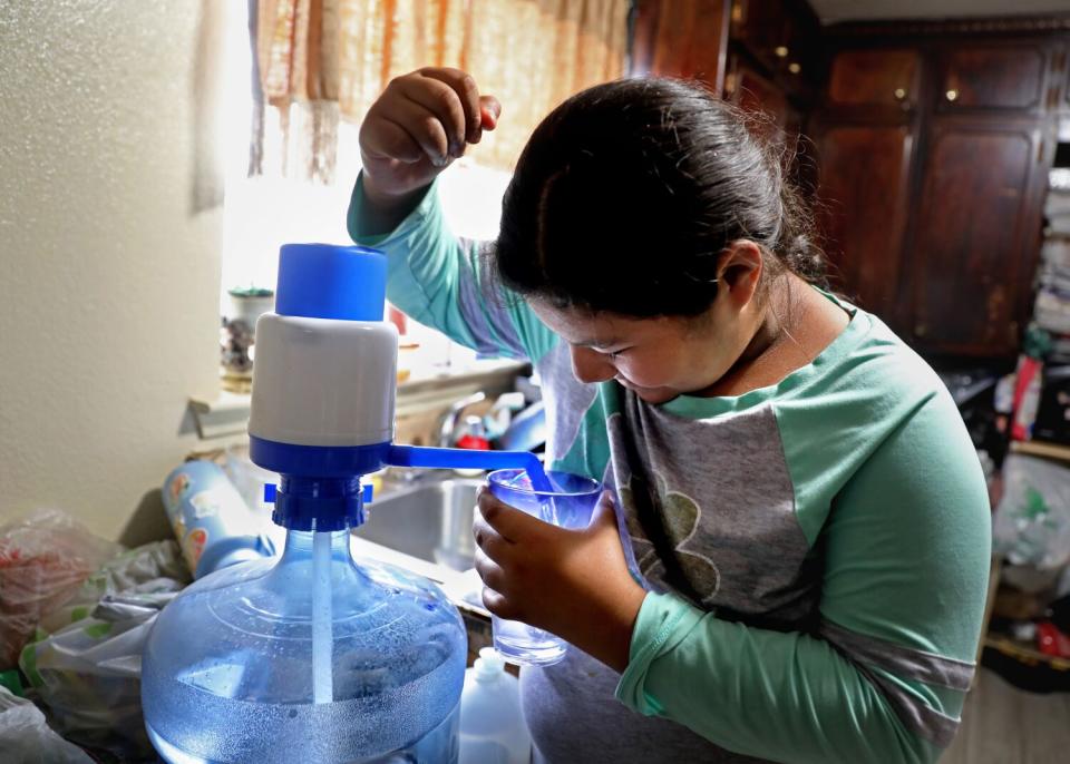 A girl pumping water from a delivery bottle into a plastic cup