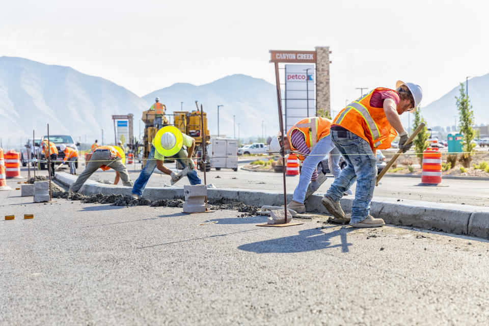 Spanish Fork, UT, USA – August 3, 2017: Road construction worker scoups up concrete while cleaning up a center medium just laid in Spanish Fork, Utah. Other workers smooth out the center medium with a float