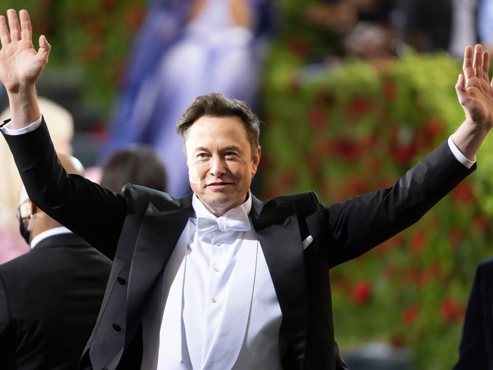 Elon Musk greets onlookers with both hands waving, at the 2022 Met Gala