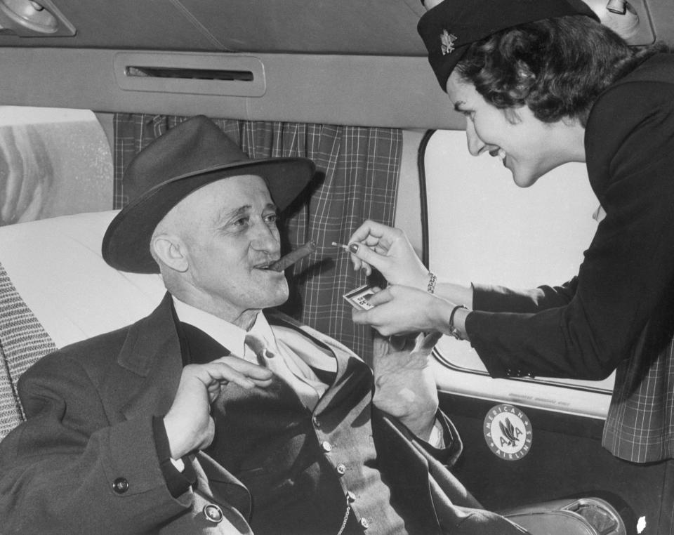 Stewardess Jane Driscoll lights a cigar for airline passenger Carl Graulein, 68, of East St. Louis, as he prepares to depart for his native Germany aboard an American Airlines overseas flight on Nov. 10, 1949.