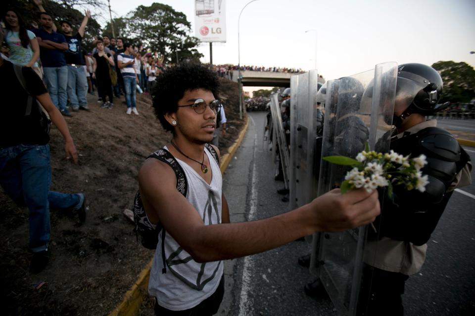 A student offers a small bouquet of flowers to police officers during a protest in Caracas, Venezuela, Friday, Feb. 14, 2014. Students are protesting the Wednesday killings of two university students who were shot in different incidents following an anti-government protest that demanded the release of student protesters who had been arrested in various parts of the country.(AP Photo/Alejandro Cegarra)