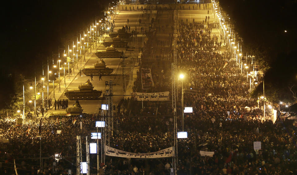 FILE - In this Tuesday, Dec. 11, 2012 file photo, Egyptian Army tanks, left, deploy as Egyptian protesters gather outside the presidential palace during a demonstration against President Mohammed Morsi in Cairo, Egypt. As Egyptians mark the third anniversary of their revolution against autocrat Hosni Mubarak in the name of democracy, there has been a powerful sign of the country’s stunning reversals since: letters of despair by some of the prominent activists who helped lead the uprising, leaked from the prisons where they are now jailed. The letters show a daunted and broken spirit, no longer speaking of imminent democracy, but of injustices and a failed struggle.(AP Photo/Hassan Ammar, File)