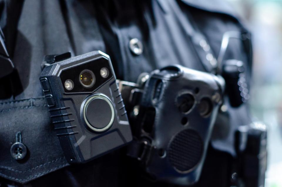 Close up of a police officer wearing a mobile video camera on the front of their uniform.