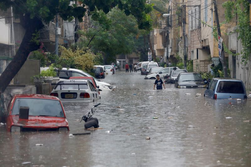 A boy wades through a flooded street with submerged vehicles during the monsoon rain, as the outbreak of the coronavirus disease (COVID-19) continues, in Karachi