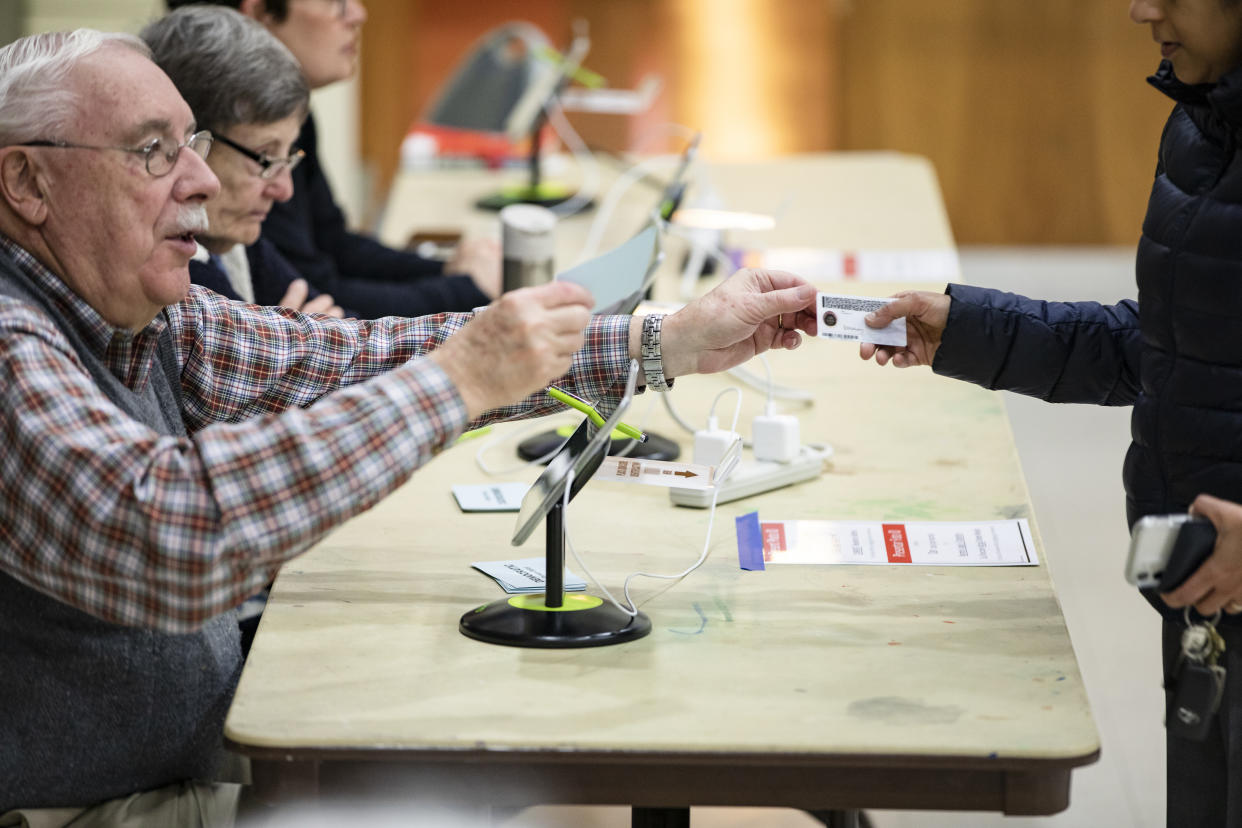 An election official hands a voter back their ID at the Madison Community Center polling place before he can cast his ballot in the Democratic presidential primary on Super Tuesday on March 3, 2020 in Arlington, VA. (Samuel Corum/Getty Images)