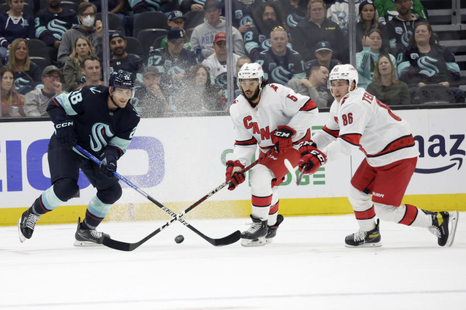 Seattle Kraken defenseman Carson Soucy (28) battes with Carolina Hurricanes defenseman Jalen Chatfield (5) and left wing Teuvo Teravainen (86) during the first period of an NHL hockey game, Monday, Oct. 17, 2022, in Seattle. (AP Photo/John Froschauer)