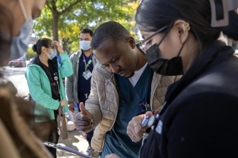 Dr. Muftawu-Deen Iddrisu checks with other members of the Mobile Migrant Health Team outside of the 1st District police station where migrants are camped, Saturday, Oct. 7, 2023, in Chicago. (AP Photo/Erin Hooley)