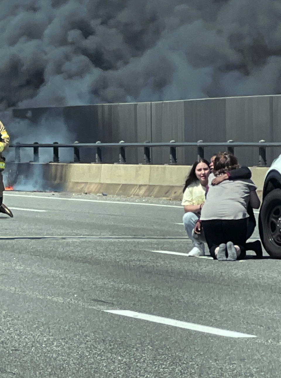 This photo provided by Angelique Feliciano shows people embracing as firefighters and police respond after a crash involving a fuel truck and a car sparked a fire on the Gold Star Bridge between New London and Groton, Conn., on Friday, April 21, 2023. The crash closed Interstate 95 in both directions during the blaze. (Angelique Feliciano via AP)