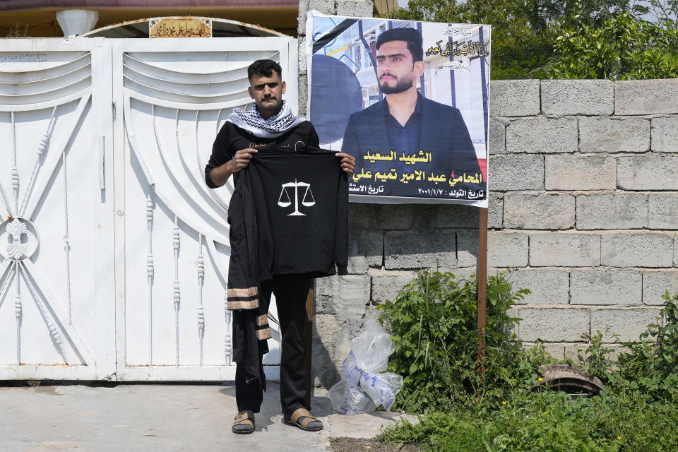 Abdullah Tamim stands next to a poster of his brother Abdel Amir Tamim while holding his brother's graduation robe in Muqdadiyah, Iraq, Wednesday, March 22, 2023. Abdel was killed in a sniper attack earlier this month. It is not known who carried out the attack. Diyala province has seen a spike in killings, some connected to sectarian hatreds but others believed linked to rivalries among Shiite factions. (AP Photo/Hadi Mizban)