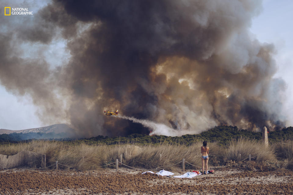 Sergej Chursyn: "A young woman in a bikini looks at an approaching forest fire near the beach. A firefighting plane drops water to extinguish the wildfire. This image was taken at the beach of Son Serra, on the island of Mallorca, on August 18, 2016."