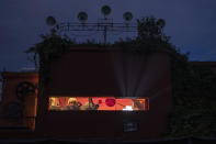 In this Saturday, May 30, 2020 photo, projector operator Pavlos Lepeniotis operates his equipment and peers out from the projection booth at the Zephyros open-air cinema that specializes in films from past decades in Athens' central Petralona district. (AP Photo/Petros Giannakouris)