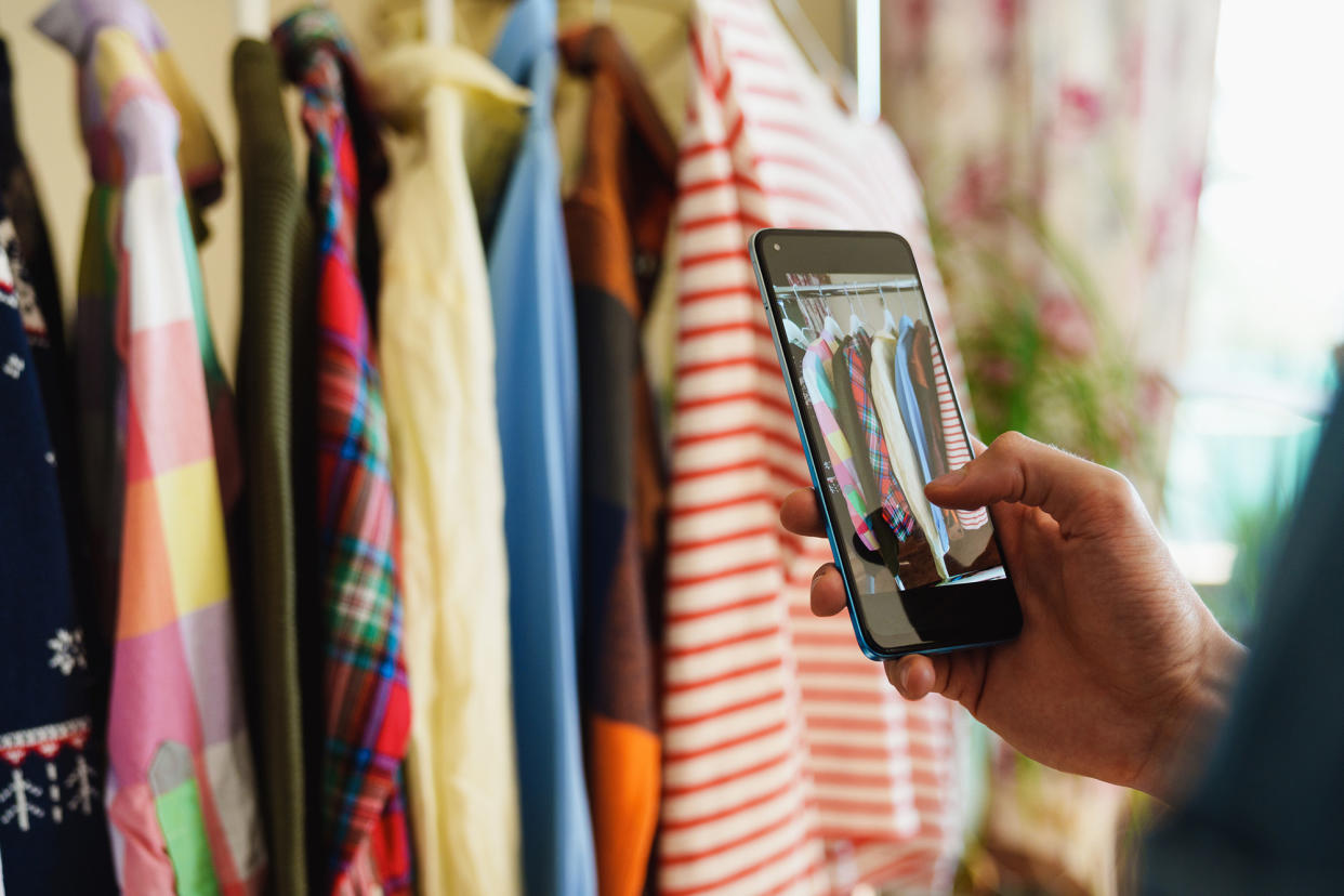 A collection of pre owned clothes hanging on a rail for resale or clothing rental, being captured in a photo using a mobile phone.