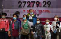 People walk in front of a bank electronic board showing the Hong Kong share index at Hong Kong Stock Exchange Friday, Feb. 21, 2020. Asian stock markets have followed Wall Street lower after a rise in virus cases in South Korea refueled investor anxiety about China's disease outbreak. (AP Photo/Vincent Yu)