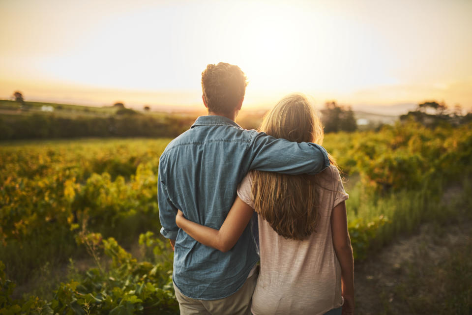 Shot of a young couple walking through their crops while holding each other and looking into the horizon