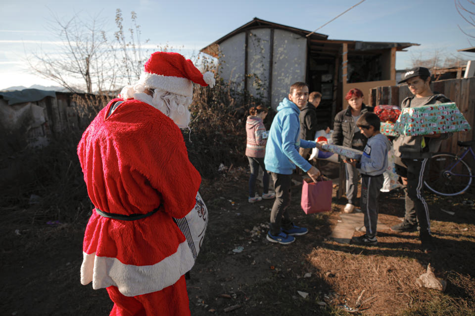 In this photo taken on Sunday, Dec. 15, 2019, Florin Catanescu, 41, center right, caries presents for a poor family, along with a youngster he looks after wearing a Santa Claus outfit, on the outskirts of Brasov, Romania. Thirty years after the 1989 death of Romania's communist-era dictator, the country is still grappling with the ugly legacy of its once-horrific orphanages. Now some of those who grew up abused and unloved in those failed institutions are turning their trauma into commitment. Florin Catanescu, who lived in an orphanage until 1997, now runs a transition home helping those leaving state care to have a better chance of leading meaningful lives. (AP Photo/Vadim Ghirda)