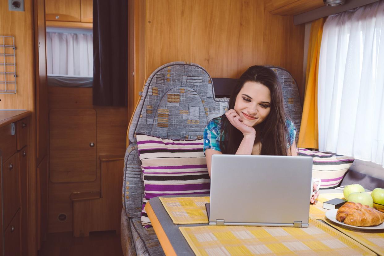 happy woman using laptop in kitchen of campervan