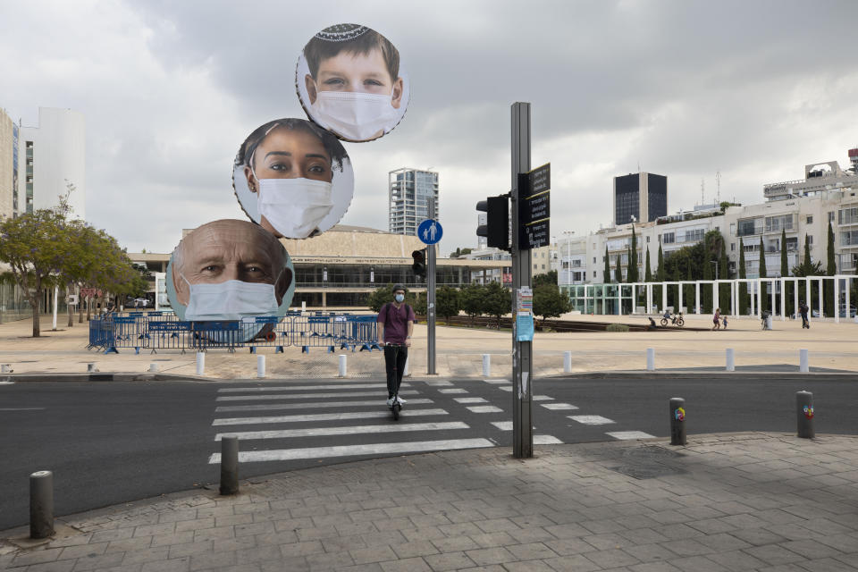 An Israeli woman rides past banners encouraging people to wear face masks in Tel Aviv, Israel, Thursday, Sept. 24, 2020. Israeli Prime Minister Benjamin Netanyahu on Wednesday announced plans for a strict, two-week nationwide lockdown in a bid to slow a raging coronavirus outbreak. (AP Photo/Sebastian Scheiner)