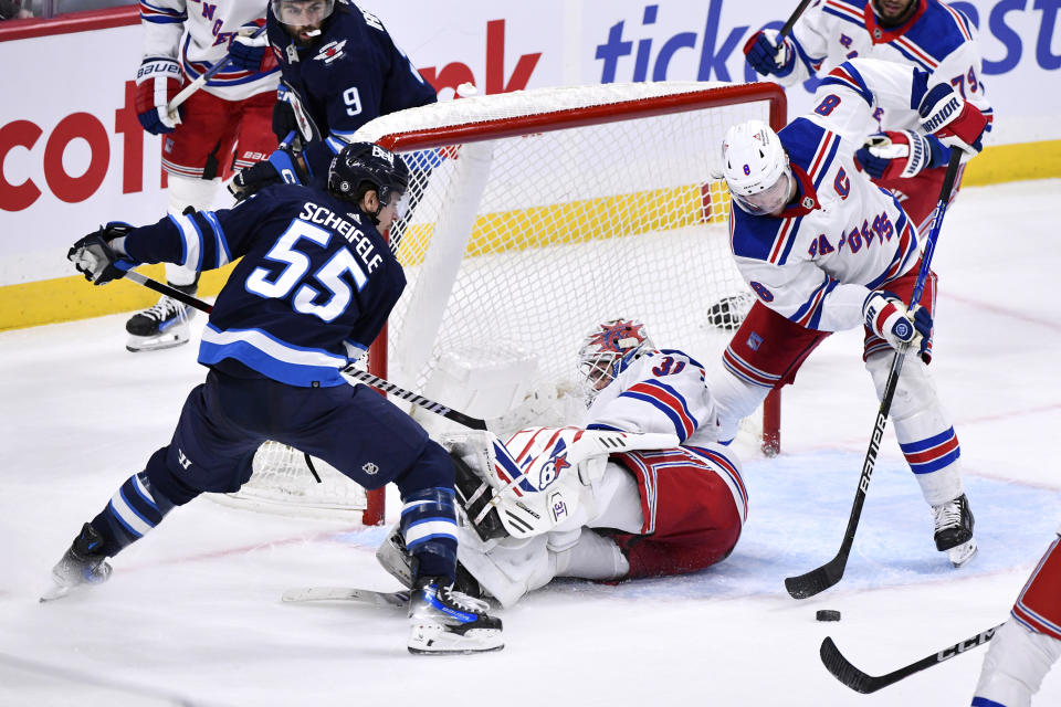 New York Rangers' Jacob Trouba (8) clears the puck from behind Rangers goaltender Igor Shesterkin (31) as Winnipeg Jets' Mark Scheifele (55) looks for a rebound during third-period NHL hockey game action in Winnipeg, Manitoba, Monday, Oct. 30, 2023. (Fred Greenslade/The Canadian Press via AP)