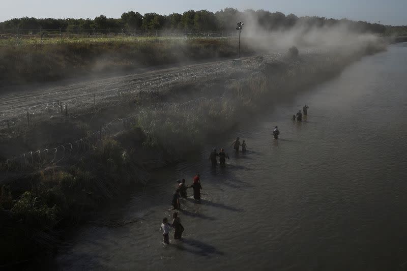 Dust rises over migrants wading the Rio Grande river in Eagle Pass
