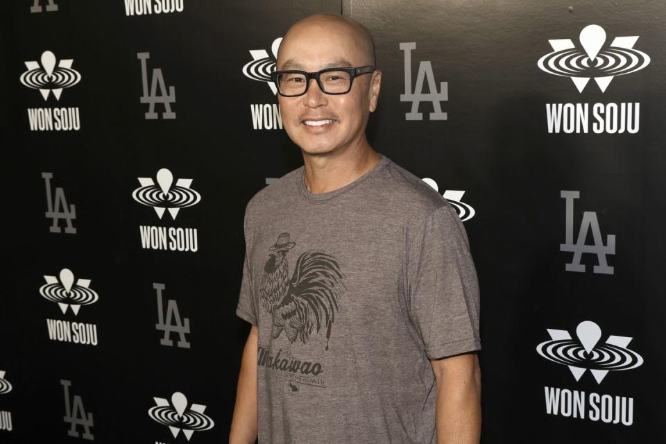 cs lee poses on the carpet wearing a taupe t shirt and black square glasses