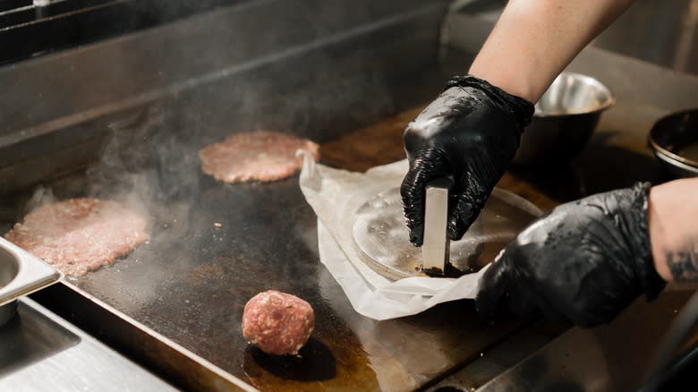 hands smashing burger on griddle