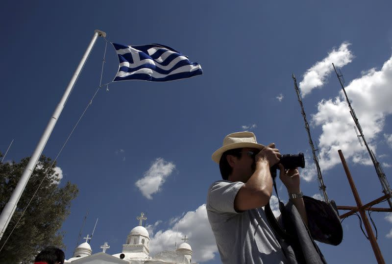 A tourist takes pictures as a Greek national flag flutters above the Orthodox church of Saint George, atop Lycabetus hill in Athens, April 22, 2015. REUTERS/Kostas Tsironis