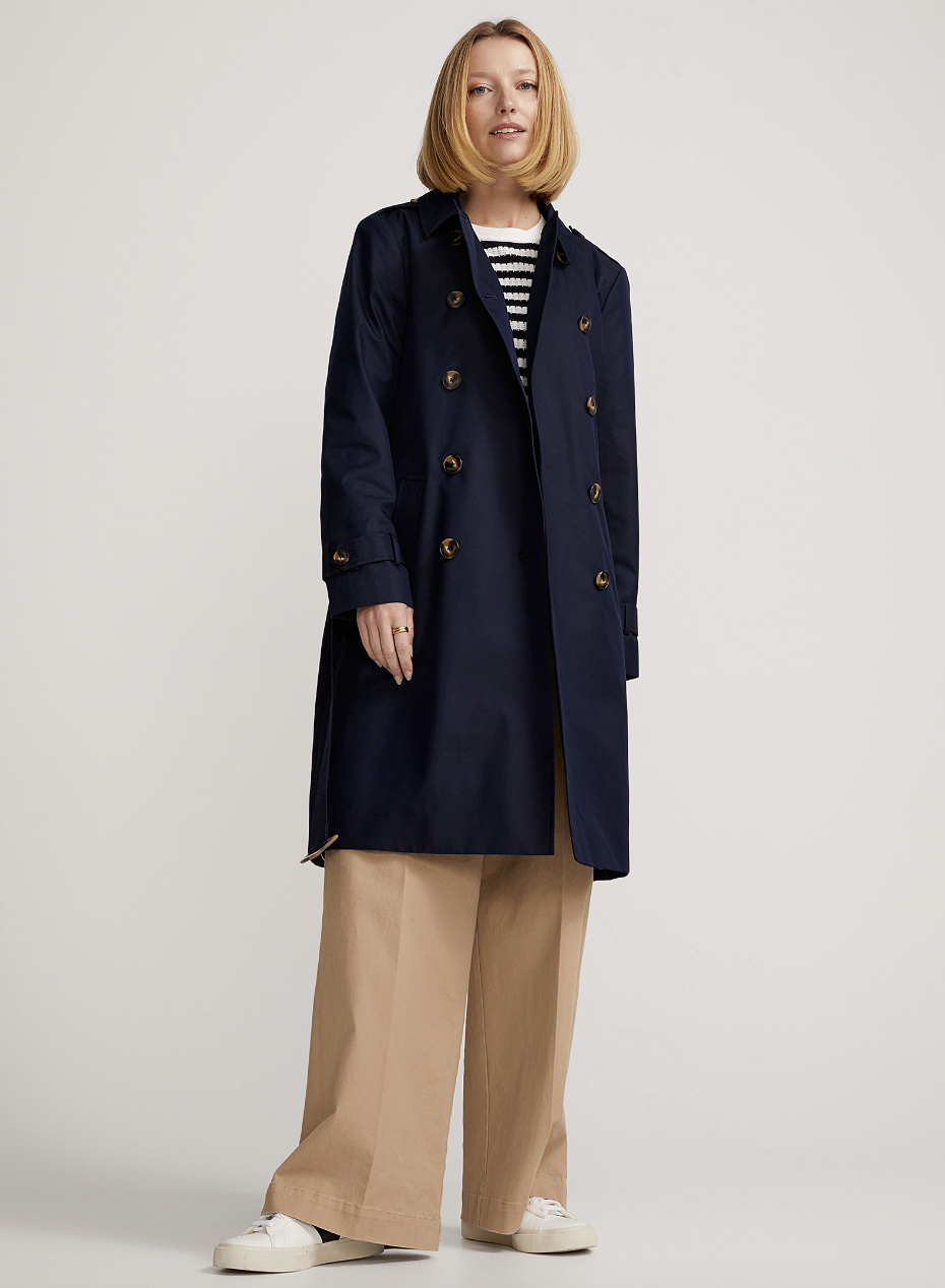 blonde model wearing wide leg beige pants and navy blue Belted Double-Breasted Trench Coat (photo via Simons)