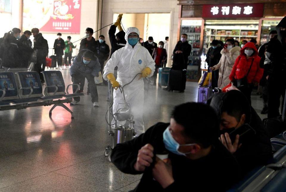 Los pasajeros reaccionan mientras un trabajador con traje de protección desinfecta la zona de salidas de la estación de tren de Hefei, en la provincia oriental china de Anhui, el 4 de marzo de 2020.