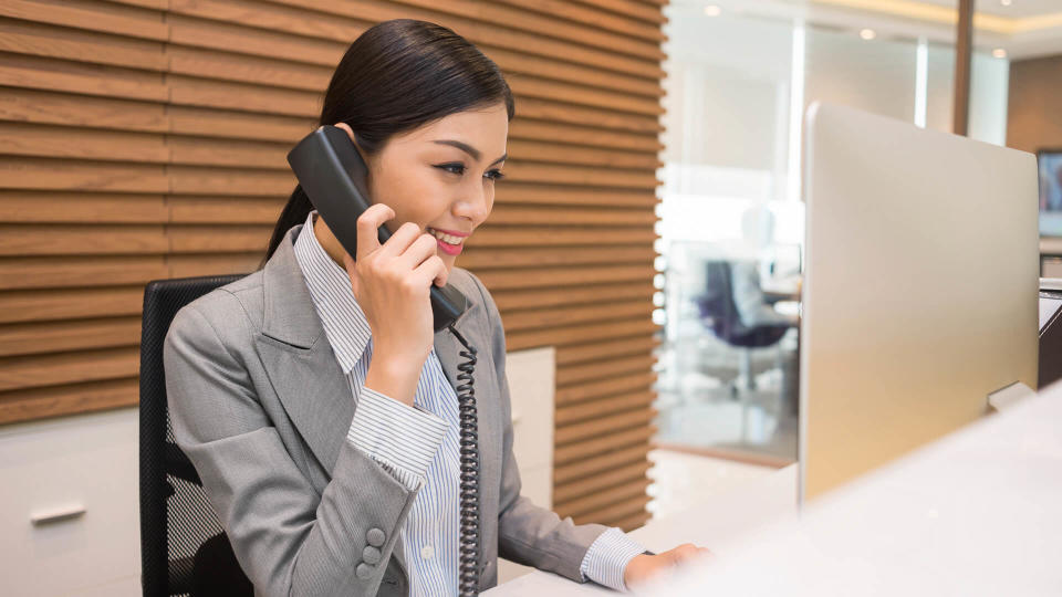 Pretty Vietnamese receptionist talking on telephone at her workplace.