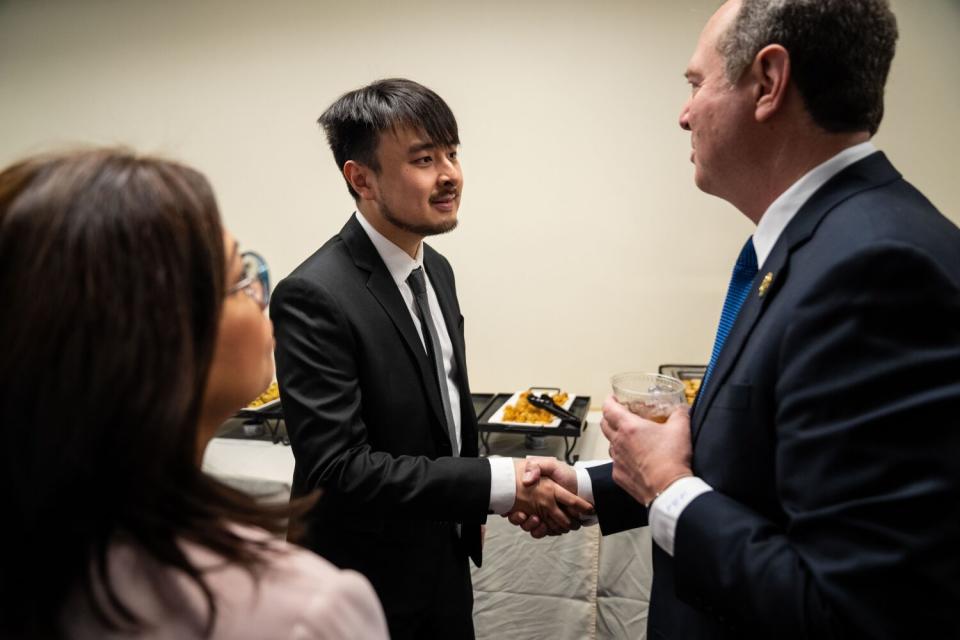 Two people shake hands as another person watches.