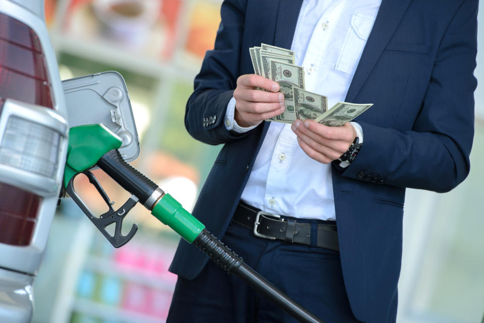 A man counting money while filling up a gas tank.