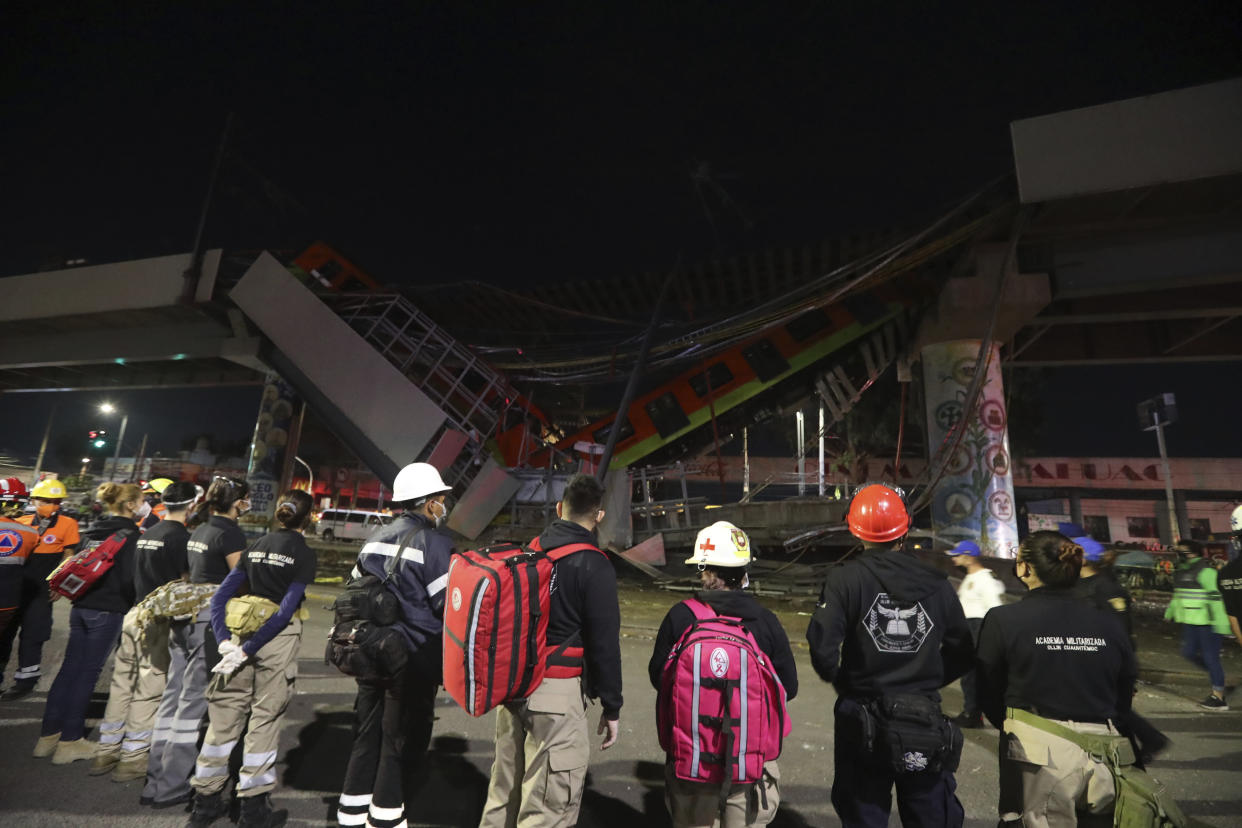 Rescue personnel stand in front of Mexico City subway cars laying at an angle after a section of Line 12 of the subway collapsed in Mexico City, Tuesday, May 4, 2021. The section passing over a road in southern Mexico City collapsed Monday night, dropping a subway train, trapping cars and causing at least 50 injuries, authorities said. (AP Photo/Marco Ugarte)