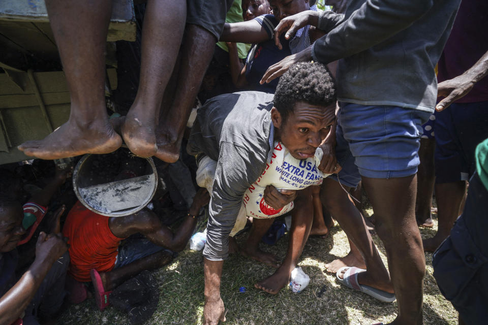 FILE - A resident crawls away with a donated bag of rice after residents temporarily overtook a truck loaded with relief supplies, in Vye Terre, Haiti, Aug. 20, 2021, six days after a 7.2 magnitude earthquake hit the area that destroyed tens of thousands of homes and killed more than 2,200 people. The country also is struggling to cope with the recent arrival of more than 12,000 deported Haitians, the majority from the U.S. (AP Photo/Fernando Llano, File)