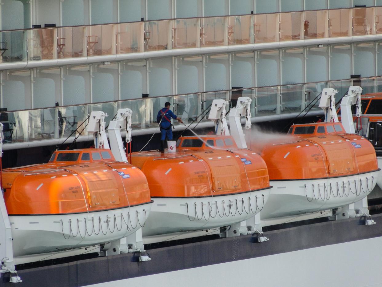 A Man is pressure washing life raft from a cruise liner.