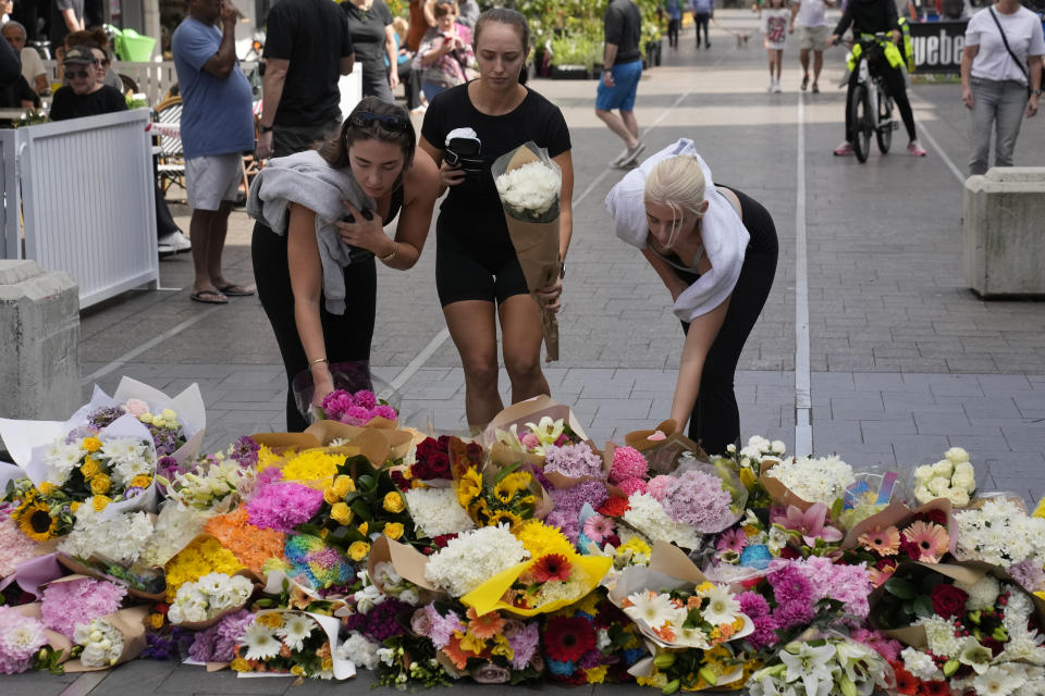 Three women place flowers as a tribute near a crime scene at Bondi Junction in Sydney, Sunday, April 14, 2024, after several people were stabbed to death at a shopping center Saturday. Police have identified Joel Cauchi, 40, as the assailant that stabbed several people to death at a busy Sydney shopping center Saturday before he was fatally shot by a police officer. (AP Photo/Rick Rycroft)