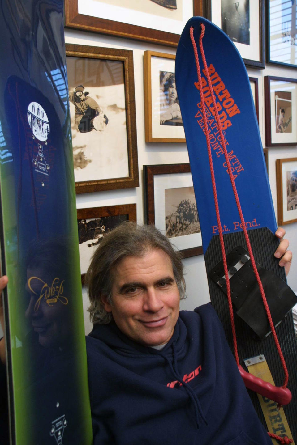 FILE - In this March 8, 2002, file photo, Jake Burton Carpenter, owner of Burton Snowboards, shows an early model, right, and one of the newer snowboards, left, in his office in Burlington, Vt. Carpenter, the innovator who brought the snowboard to the masses and helped turn the sport into a billion-dollar business, has died after a recurring bout with cancer. He was 65. Officials from the company he founded, Burton Snowboards, told The Associated Press of his death Thursday, Nov. 21, 2019. (AP Photo/Alden Pellett, File)