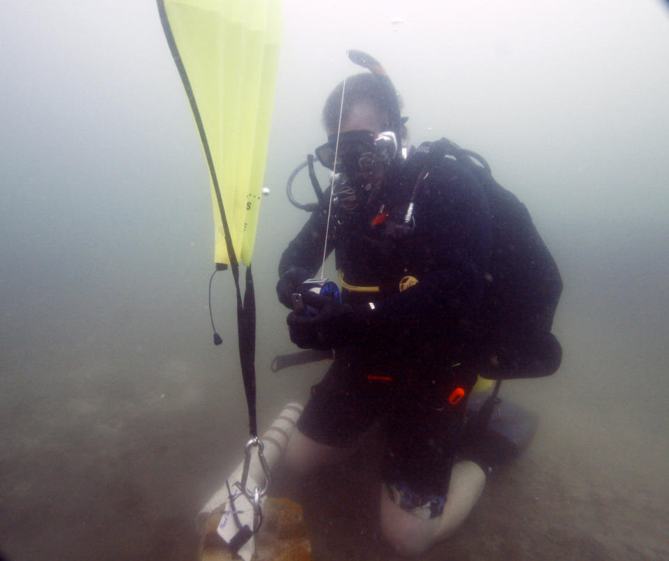 In this Saturday, Jan. 14, 2012 photo, Kenny Jenkins uses a lift bag to place a weight and geocache marker in about 33 ft. of water in Lake Denton in Avon Park Fla. Interest in geocaching has grown significantly over the years. But combining the two hobbies, geocaching and scuba diving, has only recently taken off. About 100 geocaches around the world today are only accessible with scuba gear, according to the geocaching.com database. Scuba or underwater geocaching follows the same rules as the terrestrial-based game, but includes some challenges. Land-based geocaching relies largely on GPS coordinates. With underwater geocaching, visual clues are added because it’s difficult to give an exact GPS location on the water. The cache must also be submersible and must withstand water pressure and corrosion; logbooks are waterproof. (AP Photo/Wilfredo Lee)