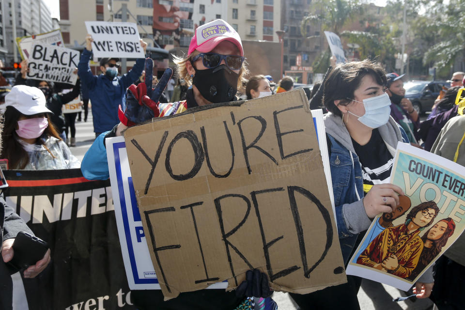 A person celebrating in the streets of Los Angeles holds a sign saying 'you're fired', in reference to Donald Trump's catchphrase.