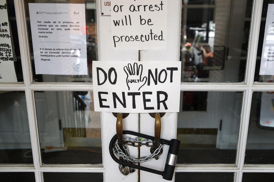 Signs hang on the chained front door to the shuttered Venezuelan Embassy, Thursday, April 25, 2019, in Washington. Activists have been staging a round-the-clock vigil inside the embassy, occupying it to prevent representatives of Juan Guiado, opposition leader and self-proclaimed interim president, from taking over the building. (AP Photo/Patrick Semansky)