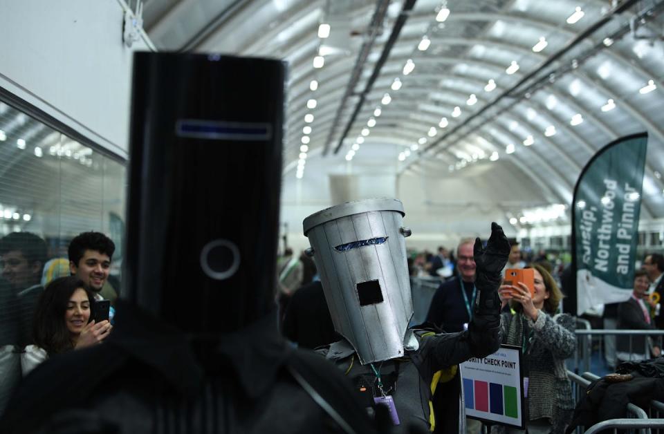 A person with a trash bin head gestures with his thumbs down to a person with a bucket as a head.