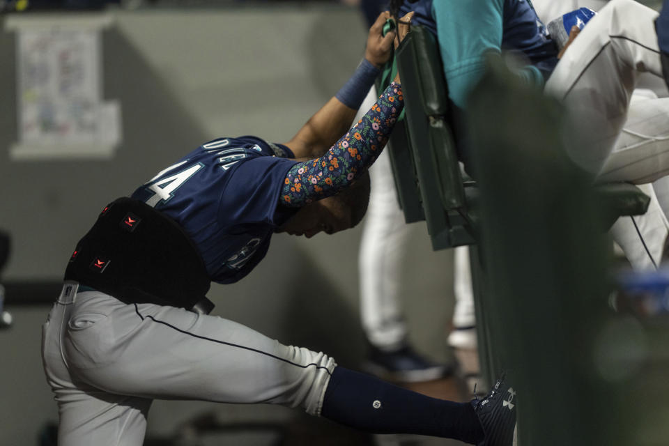 Seattle Mariners' Julio Rodriguez stretches in the dugout while wearing a device on his lower back during the fifth inning of a baseball game against the Detroit Tigers, Monday, Oct. 3, 2022, in Seattle. (AP Photo/Stephen Brashear)