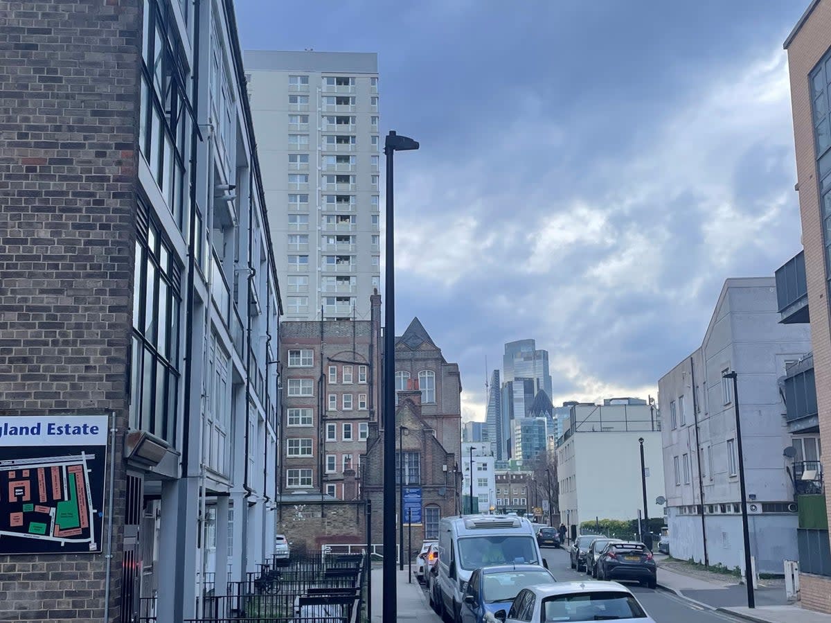 A sign for a housing estate in Shadwell, London, with the skycrapers of the financial district in the background (The Independent)