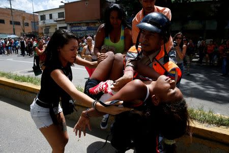 A police officer carries a woman who fainted while gathering to try to buy pasta outside a supermarket in Caracas, Venezuela, June 10, 2016. REUTERS/Carlos Garcia Rawlins/File Photo