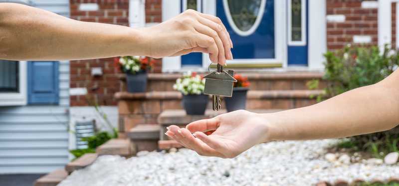 person handing house key to another person in front of new home