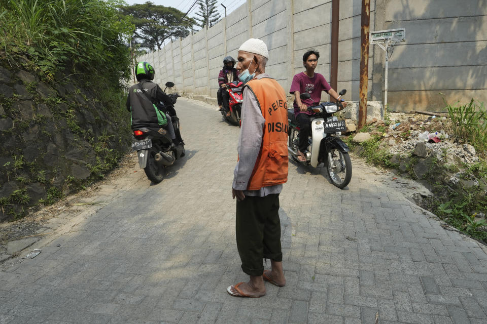 Husin bin Nisan, a volunteer traffic attendant, stands on a street where he directs traffic for a living in Tangerang, Indonesia, Monday, May 15, 2023. After spending more than three decades picking tips from motorists, the 85-year-old man is finally realizing his dream to go to the Islamic holy cities of Mecca and Medina for hajj pilgrimage. (AP Photo/Achmad Ibrahim)