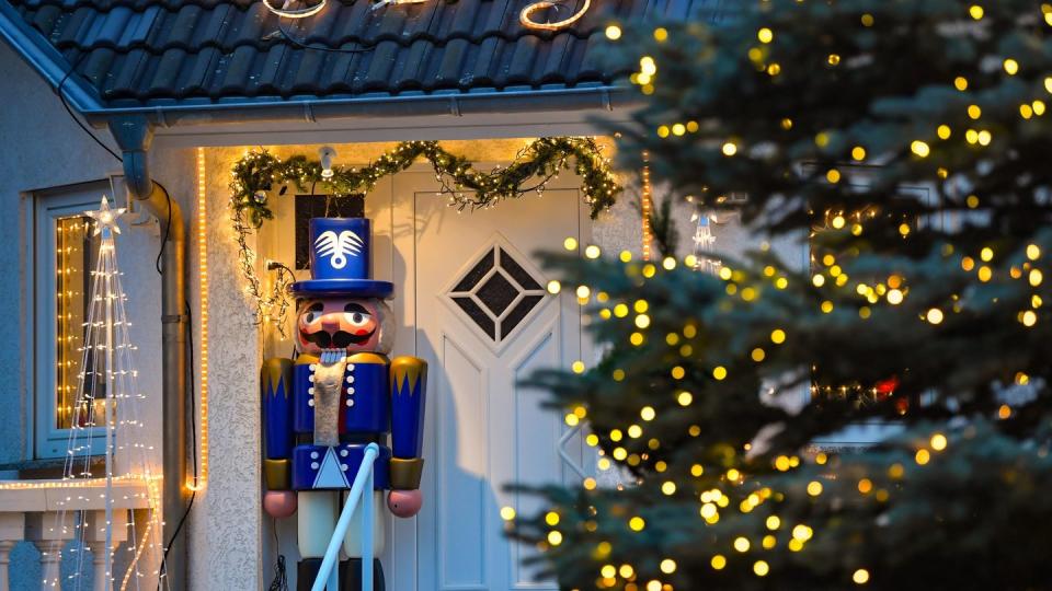 Lichterketten und ein großer Nussknacker stehen an einem weihnachtlich geschmückten Hauseingang.