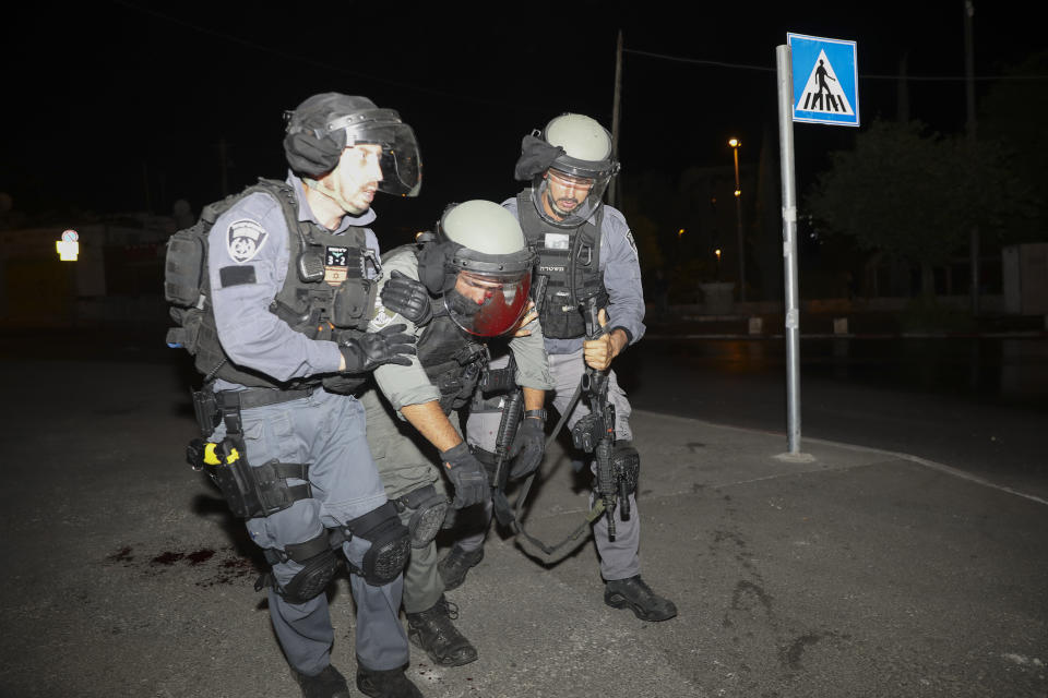 An injured Israeli police officer is helped during clashes with Palestinian protesters, in east Jerusalem, Friday, May 7, 2021. Palestinians protested following Israel's threatened eviction of dozens of Palestinians in the Sheikh Jarrah neighborhood in east Jerusalem, who have been embroiled in a long legal battle with Israeli settlers trying to acquire property in the neighborhood. (AP Photo/Mahmoud Illean)