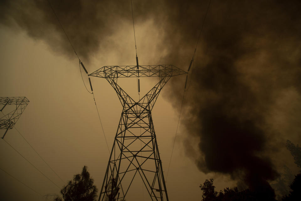 FILE - In this Nov. 9, 2018, file photo, smoke billows around power transmission lines as the Camp Fire burns in Big Bend, Calif. Experts say it's hard to know whether keeping millions of Californians in the dark prevented a catastrophic wildfire. The question takes on new significance after authorities said Friday, Oct. 11, 2019, that a man in his 60s who relied on oxygen died 12 minutes after losing electricity in a planned outage by Pacific Gas & Electric Co., east of Sacramento. (AP Photo/Noah Berger, File)
