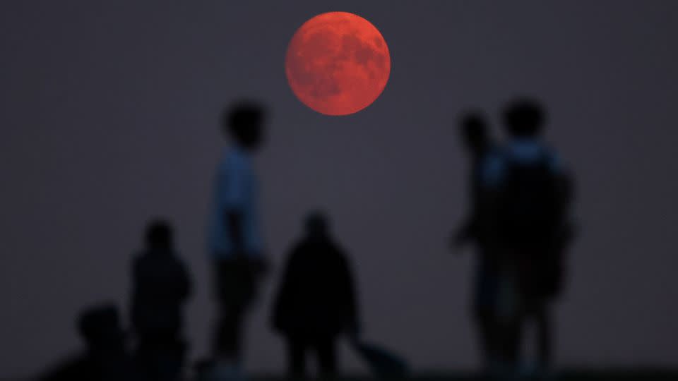 People view the moon as it rises, with a red glow attributable to smoke particles in the upper atmosphere from North American wildfires, a day ahead of the super blue moon, at Parliament Hill in London, August 18. - Toby Melville/Reuters